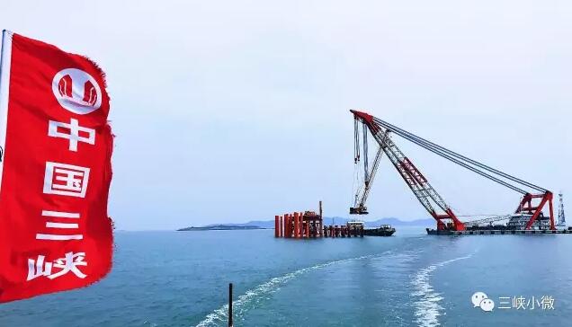 碧空如洗，白云低垂，海上一派风平浪静的景象。不远处两台已经完成吊装的风机矗立海面，洁白的机身格外醒目